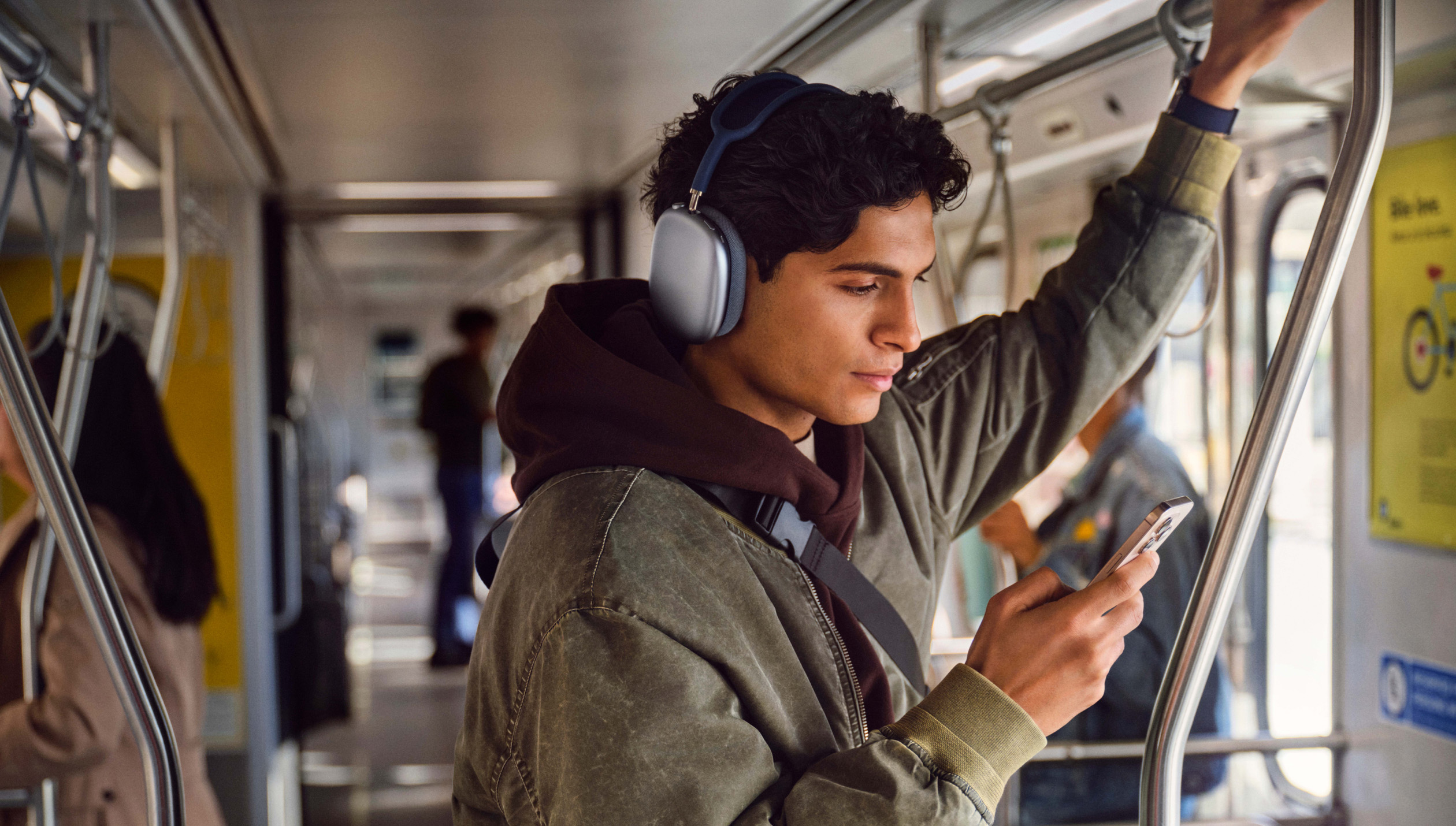 A person standing on a commuter train, looking at an iPhone while holding onto a hand rail.